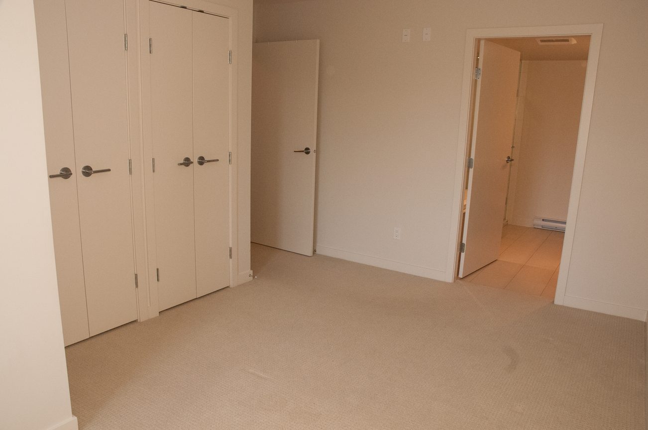 Bright living room with carpeted floors and multiple closet doors. - 507-1677 Lloyd Avenue, North Vancouver
