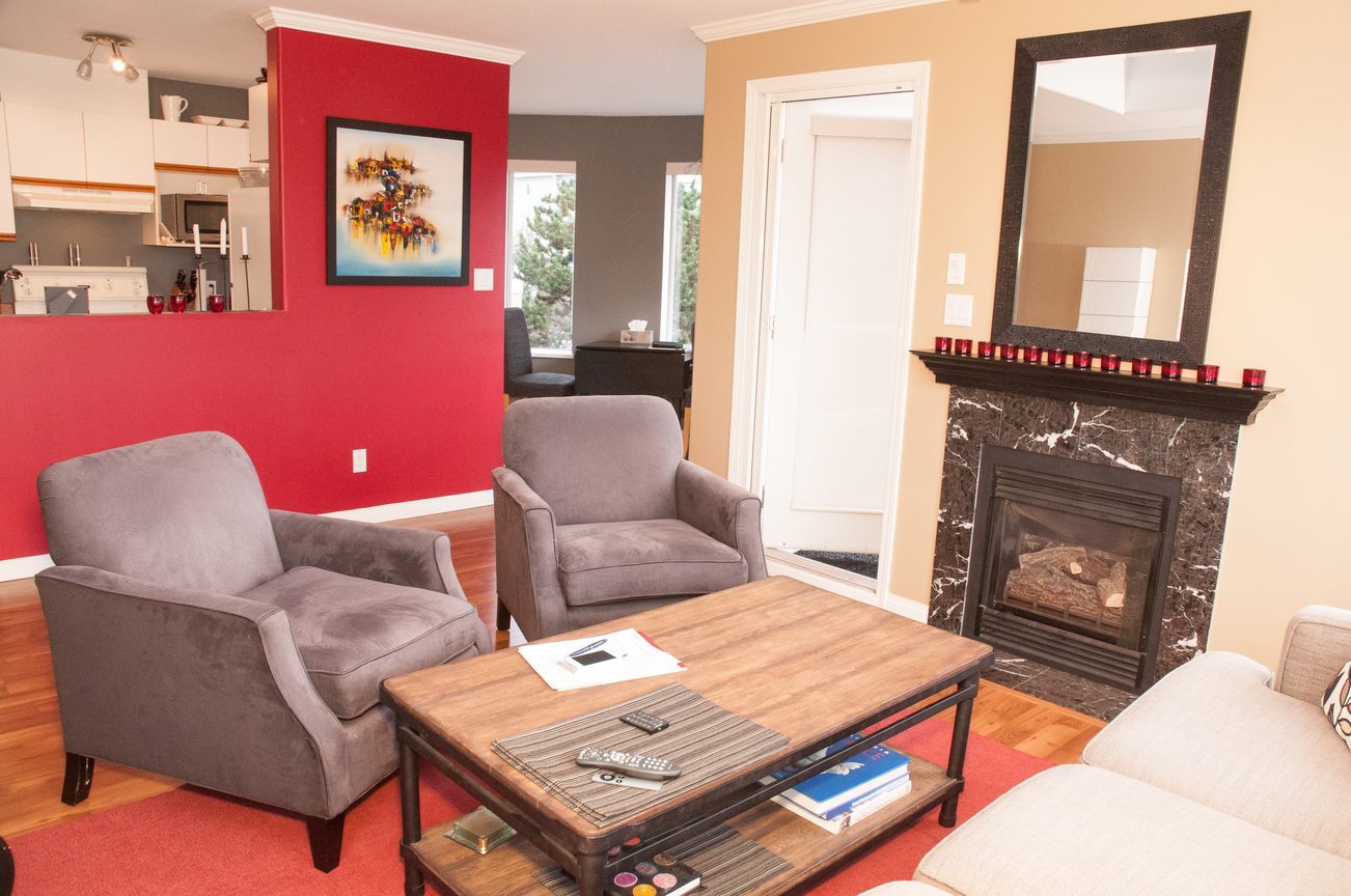 Furnished living room with red accent wall, hardwood floors, and a cozy fireplace. - 401-120 East 2nd Street, North Vancouver
