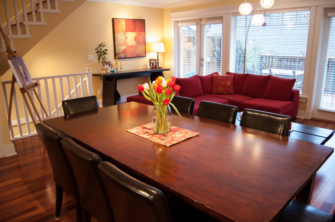 Dining room with hardwood floors, red sectional sofa, and a large wooden table. - 221 East 17th Street, North Vancouver