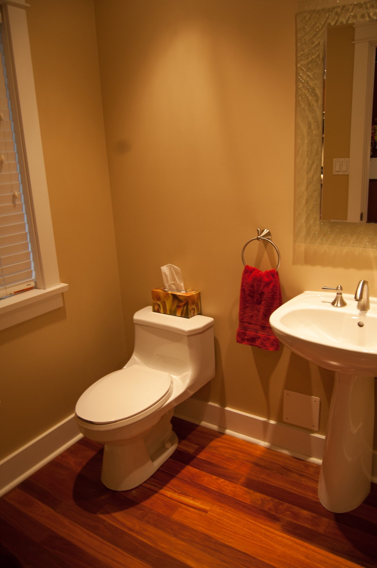 Small bathroom with hardwood floors, a white toilet, and a red towel on a ring. - 221 East 17th Street, North Vancouver