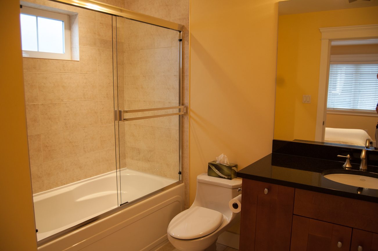 Bathroom with dark countertops, modern shower, and tissue box on sink. - 221 East 17th Street, North Vancouver