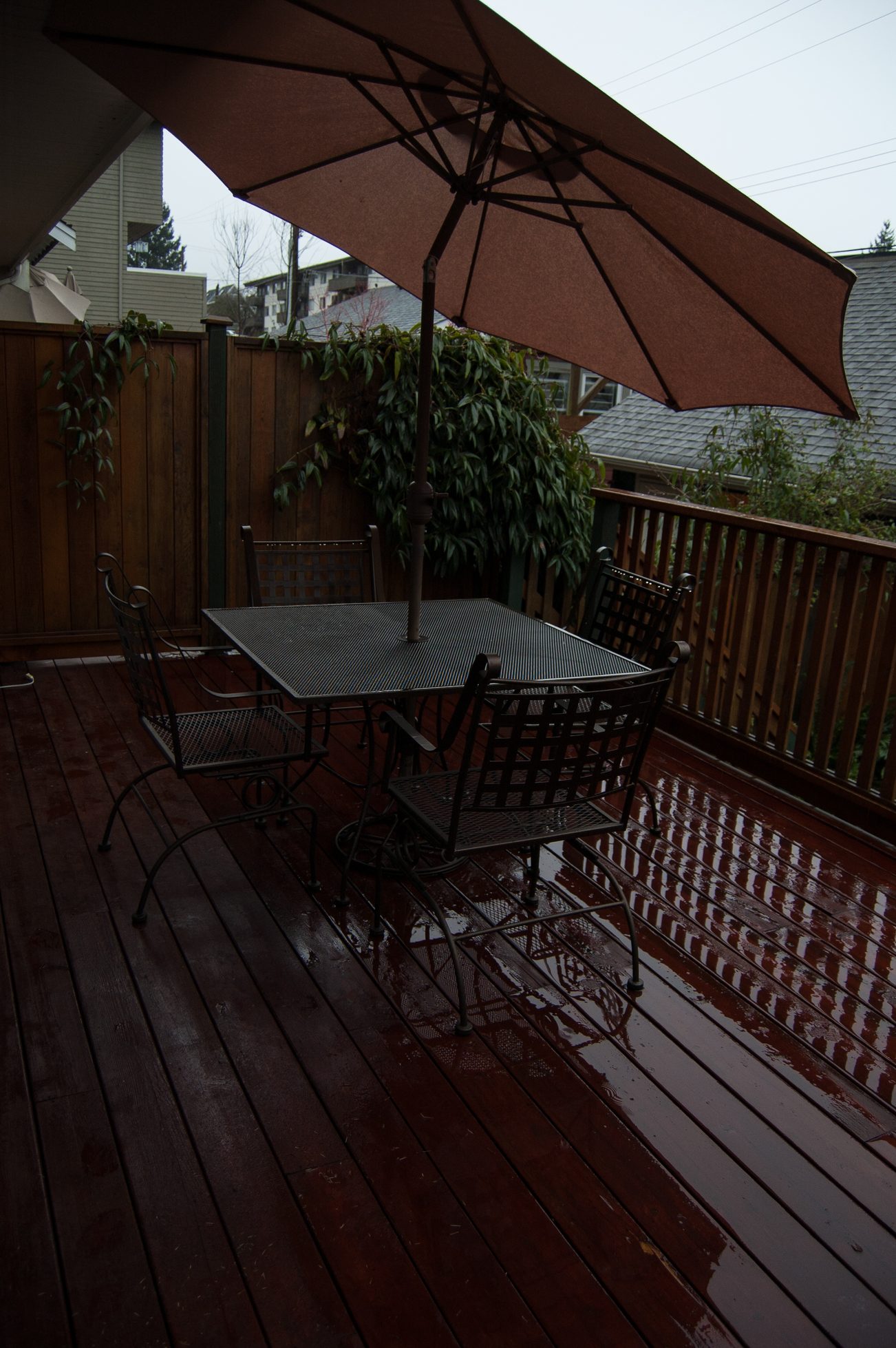 Furnished patio with wet wooden deck, outdoor table, chairs, and umbrella. - 221 East 17th Street, North Vancouver