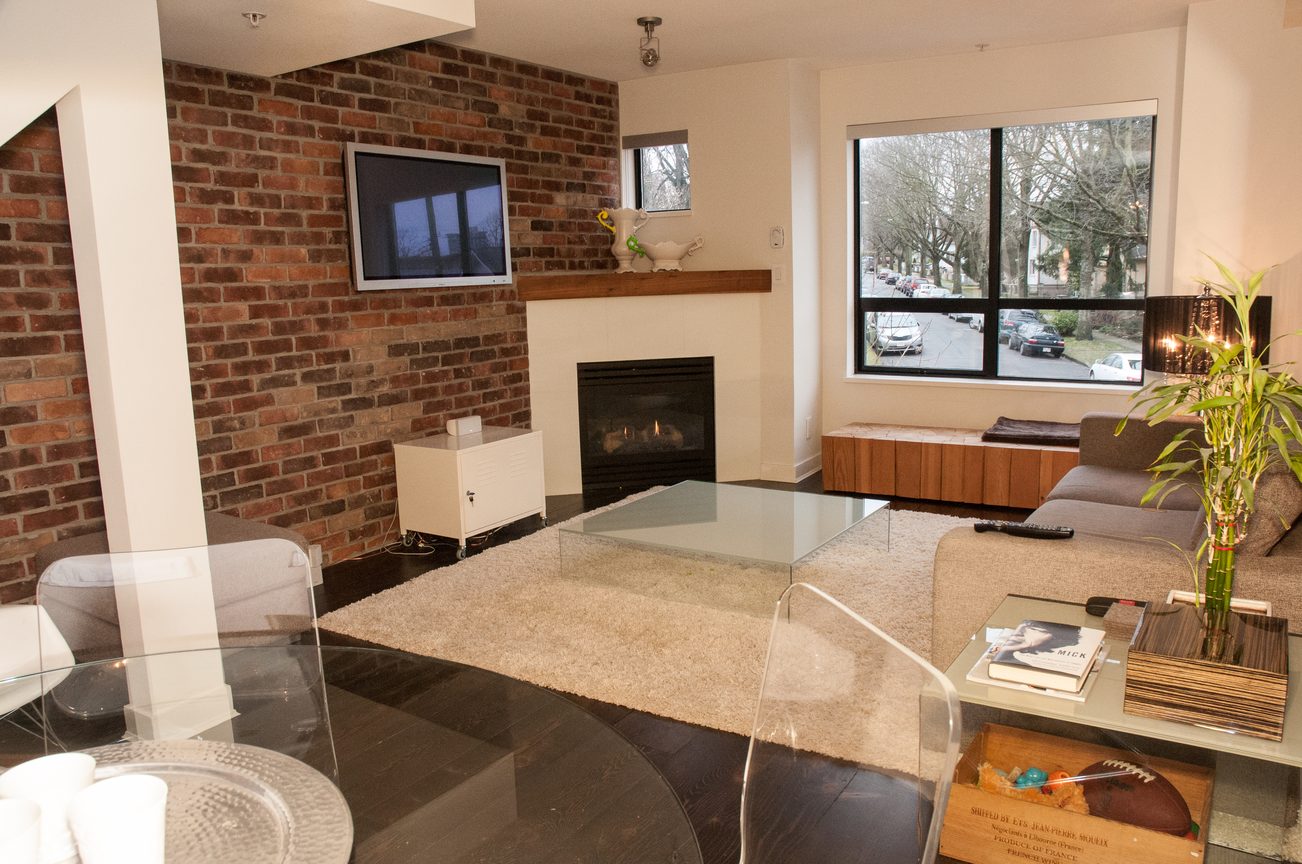 Furnished living room with brick wall, fireplace, and large window view. - 125- 1863 Stainsbury Ave, Vancouver West Side