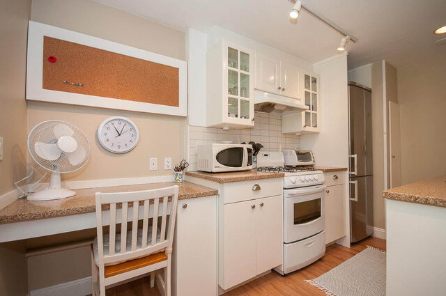 Bright kitchen with white cabinets, granite countertops, and a compact dining area featuring a white chair and desk.