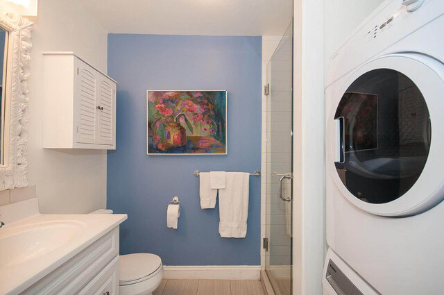 Bright bathroom with white cabinetry, blue walls, and a floral painting, featuring a bathtub and sink. - Address WITHHELD, North Vancouver