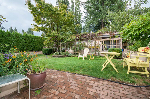 Spacious backyard with lush greenery, a brick patio, and a cozy Adirondack chair setup. - Address WITHHELD, North Vancouver