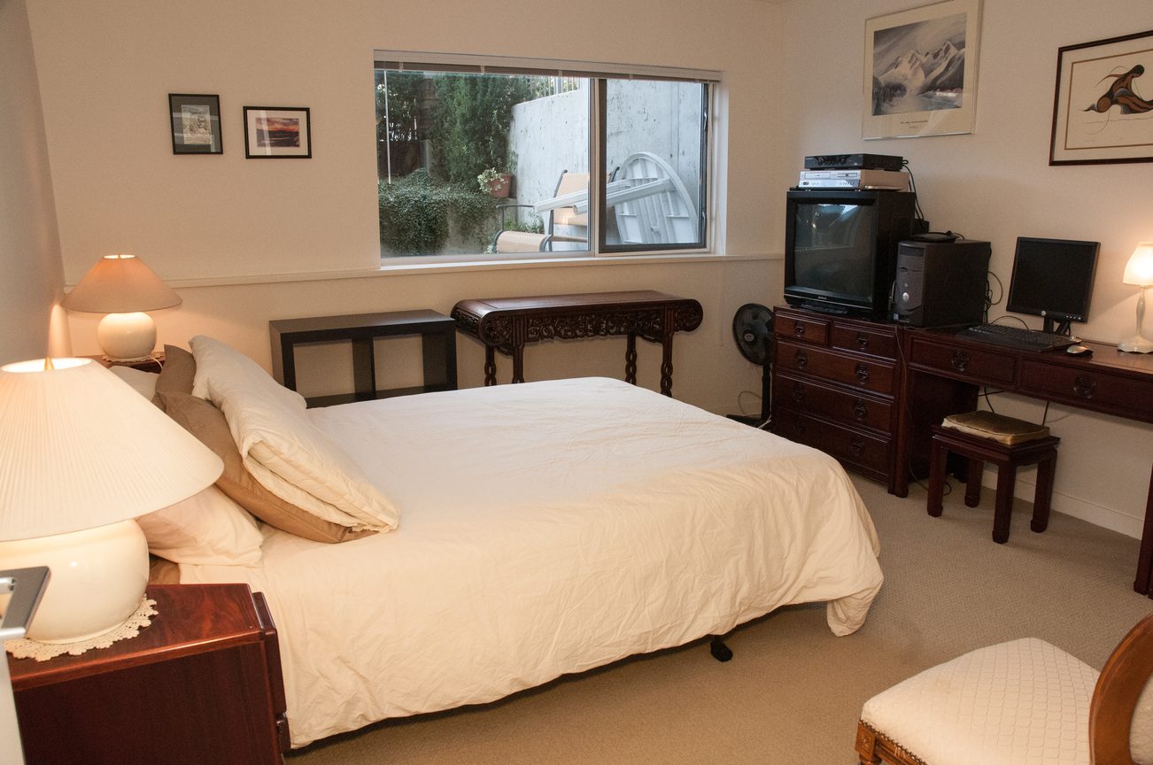Bright bedroom with wooden furniture, desk, and window view. - TH4 - 1288 Chesterfield Ave, North Vancouver