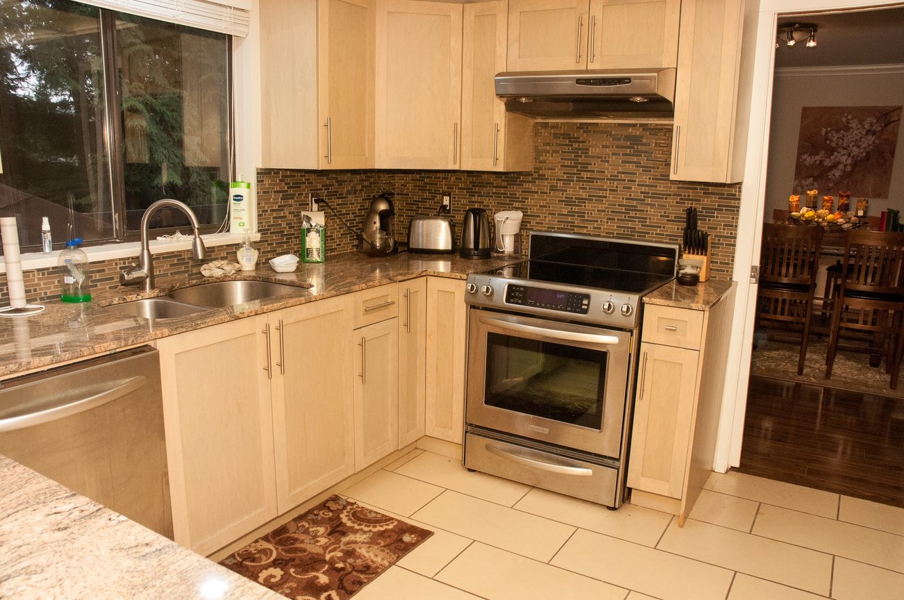 Bright kitchen with granite countertops, stainless steel appliances, and a tiled backsplash. - 5550 Huckleberry Lane, North Vancouver