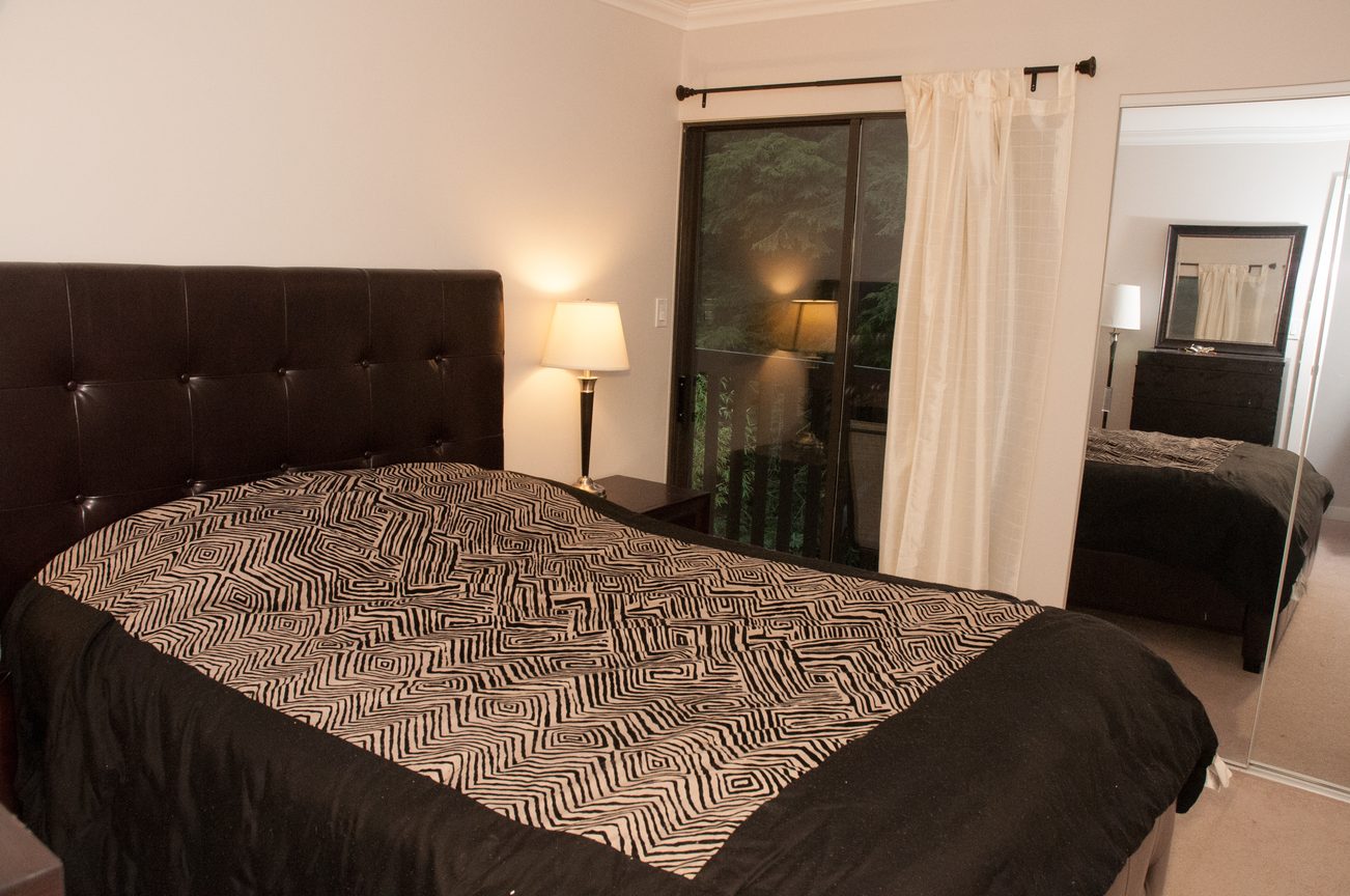 Spacious bedroom with a large bed, patterned bedding, and sliding glass door leading to a patio. - 5550 Huckleberry Lane, North Vancouver