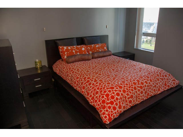 Furnished bedroom with modern furniture, orange patterned bedding, and hardwood floors. - 1501-1483 Homer Street, Vancouver Downtown