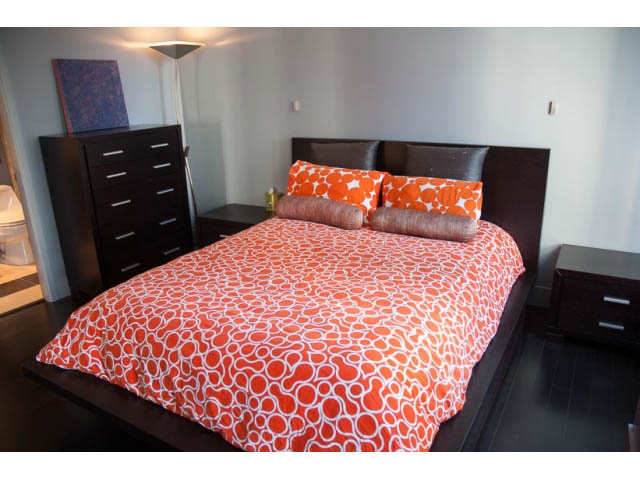 Furnished 2-bedroom + den with modern orange patterned bedding and dark wood furniture. - 1501-1483 Homer Street, Vancouver Downtown