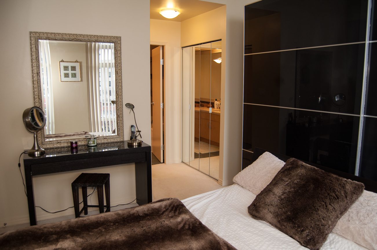 Furnished bedroom with a cozy bed, fur throw, and a sleek black vanity with a mirror. - TH A- 1199 Marinaside Cres, Vancouver Downtown