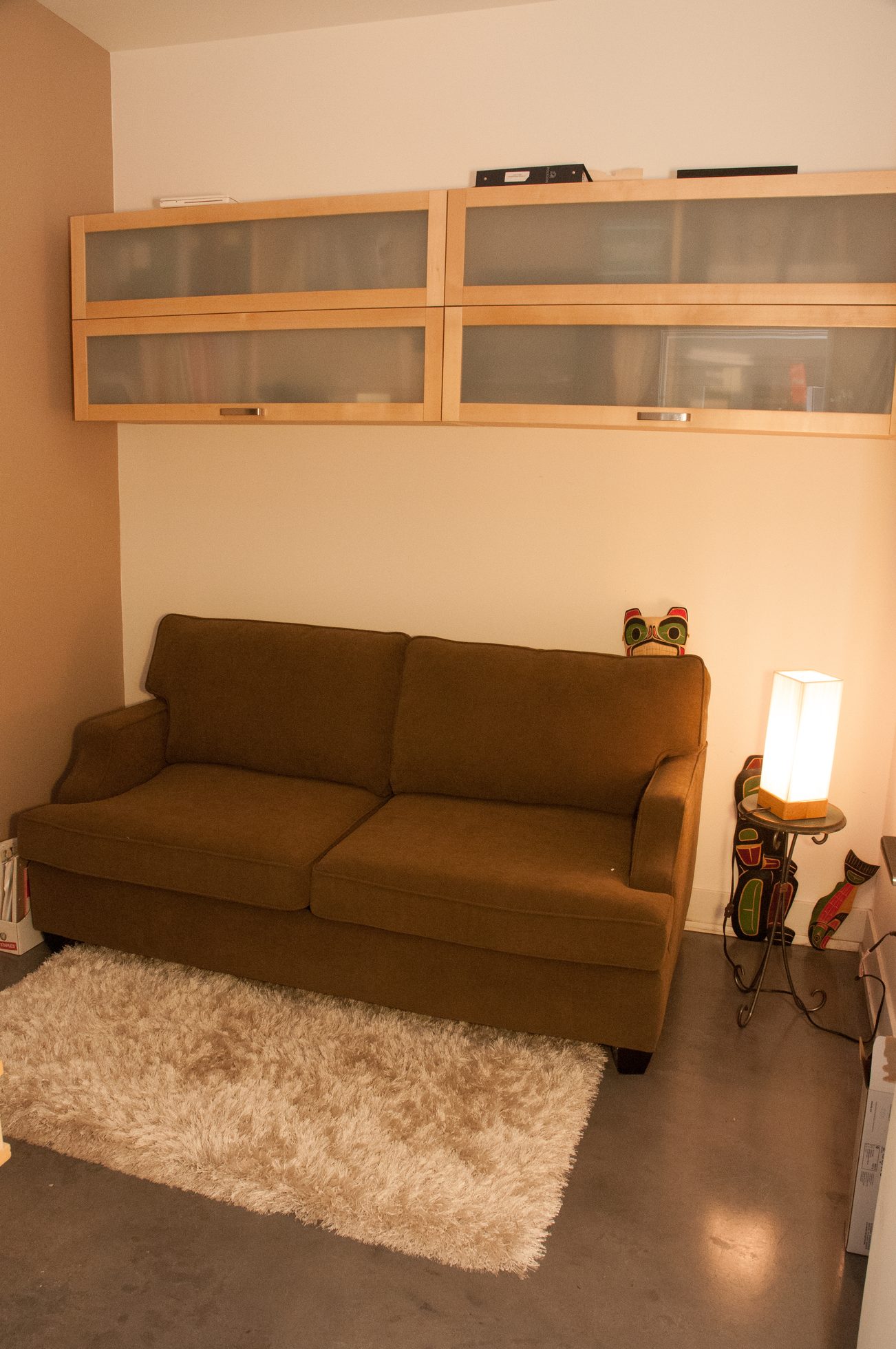 Living room with brown sofa, shag rug, and wooden cabinets above. - 306-650 Evergreen Place, North Vancouver