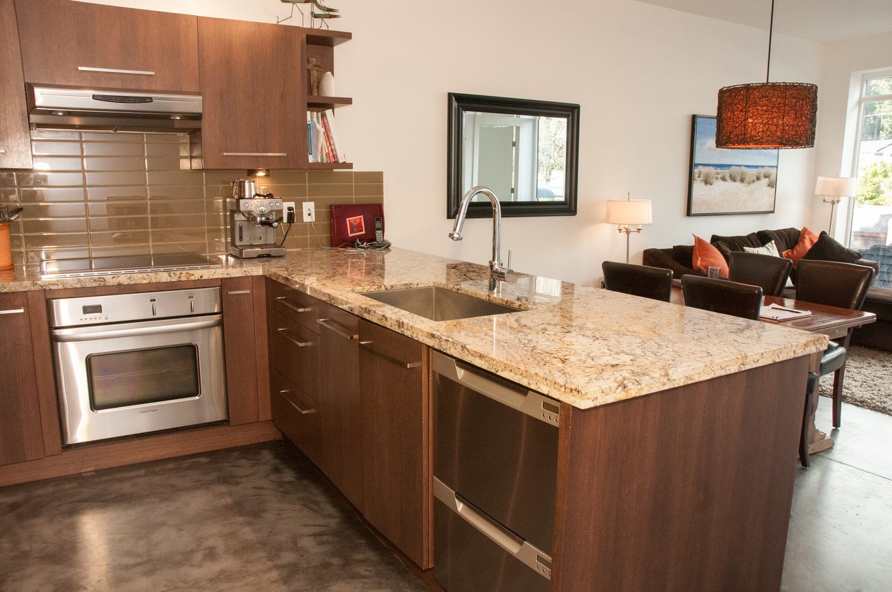 Bright kitchen with granite countertops, stainless steel appliances, and a cozy living area in the background.