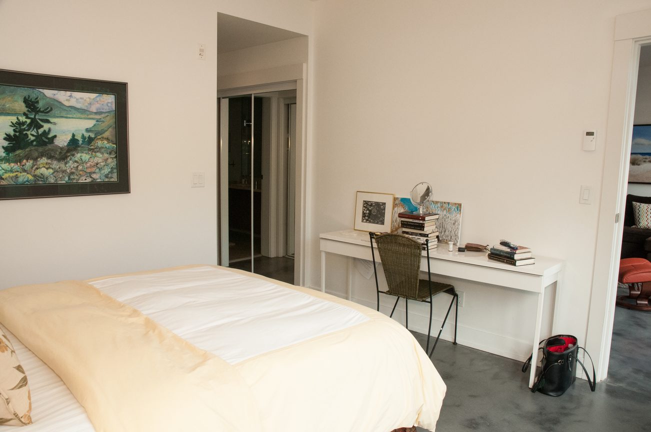 Furnished bedroom with white walls, a desk, and a large painting. - 306-650 Evergreen Place, North Vancouver