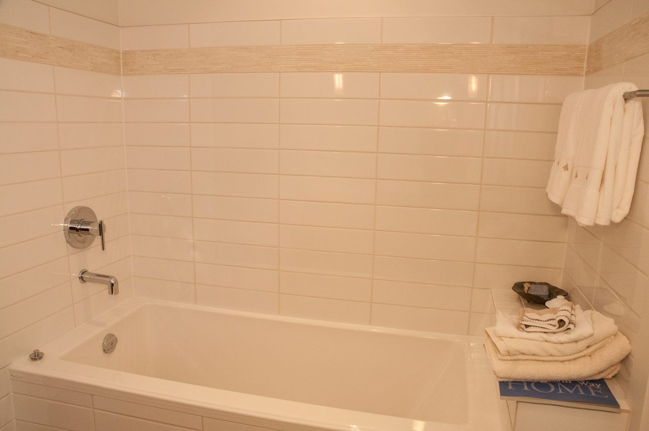 Furnished bathroom with white tiles and a bathtub, neatly arranged towels on the side. - 306-650 Evergreen Place, North Vancouver