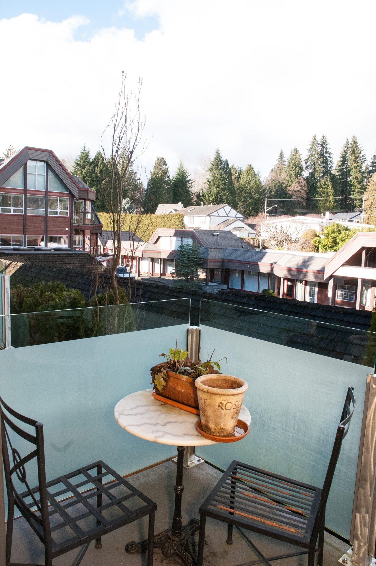Furnished balcony with glass railing, small table, and potted plants. - 306-650 Evergreen Place, North Vancouver