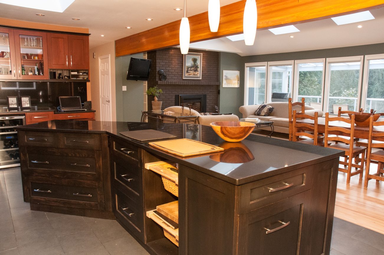 Open-concept kitchen and living area with dark wood cabinets, granite countertops, and a brick fireplace. - 5646 Westport Rd, West Vancouver