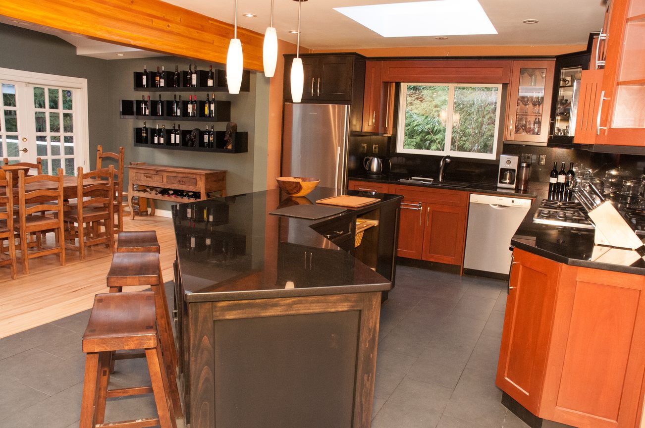 Bright kitchen with dark countertops, wooden cabinets, and a dining area with a large table and chairs. - 5646 Westport Rd, West Vancouver