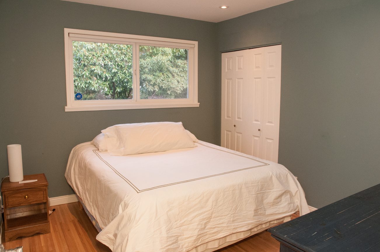 Spacious bedroom with two twin beds, hardwood floors, and a window with a view of greenery. - 5646 Westport Rd, West Vancouver
