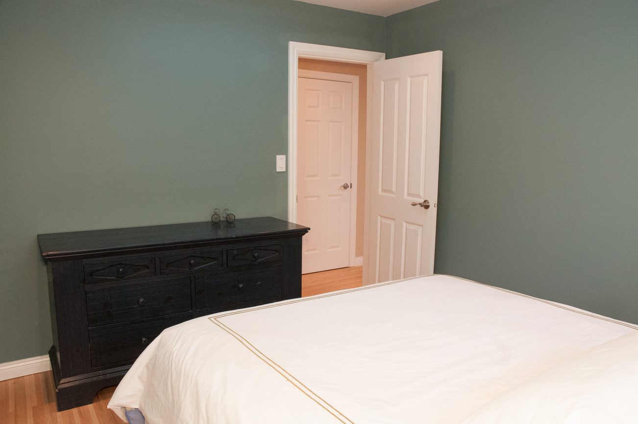 Spacious bedroom with dark wood dresser and white door. - 5646 Westport Rd, West Vancouver