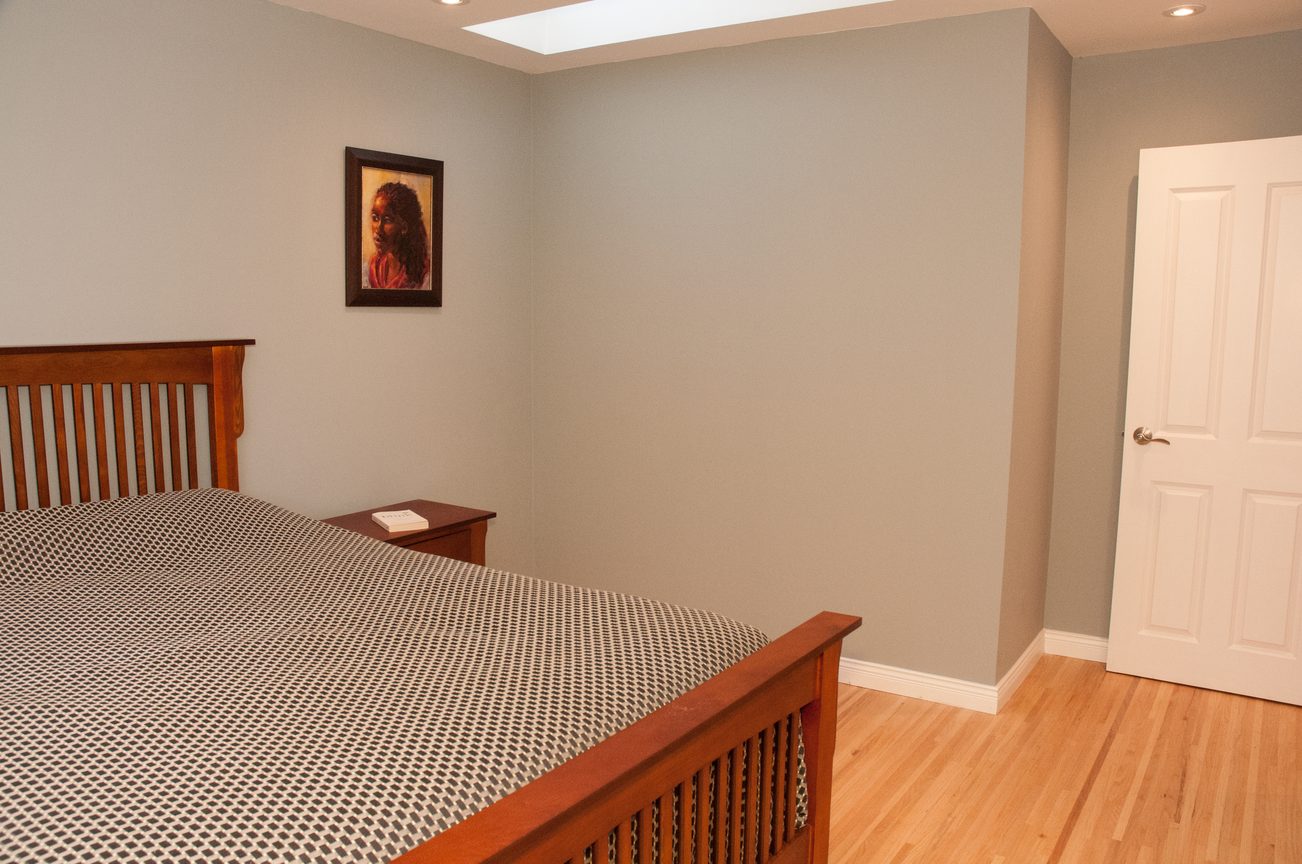 Spacious bedroom with wooden headboard, hardwood floors, and a skylight. - 5646 Westport Rd, West Vancouver