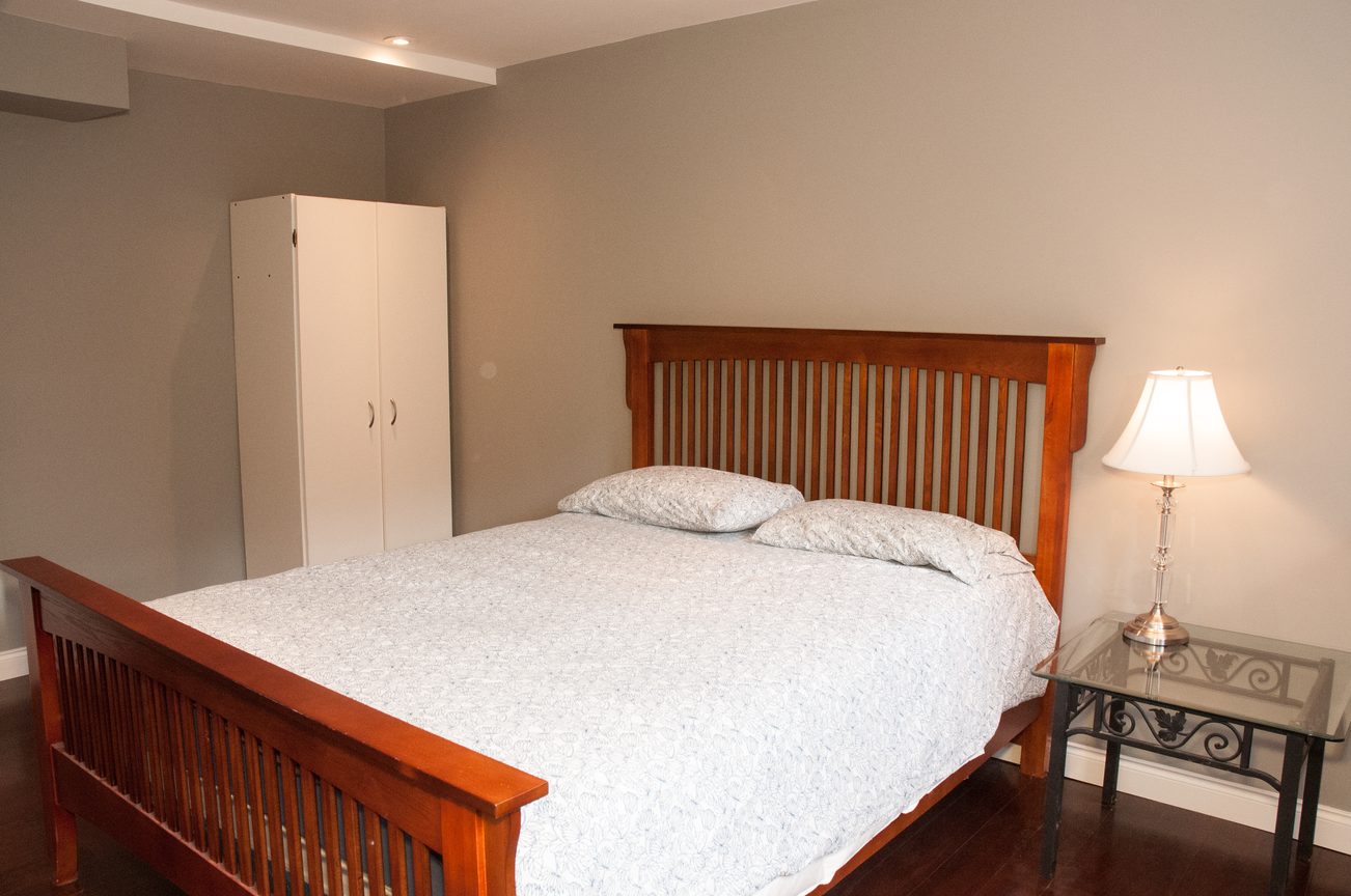 Spacious bedroom with wooden bed frame, white closet, and bedside lamp. - 5646 Westport Rd, West Vancouver