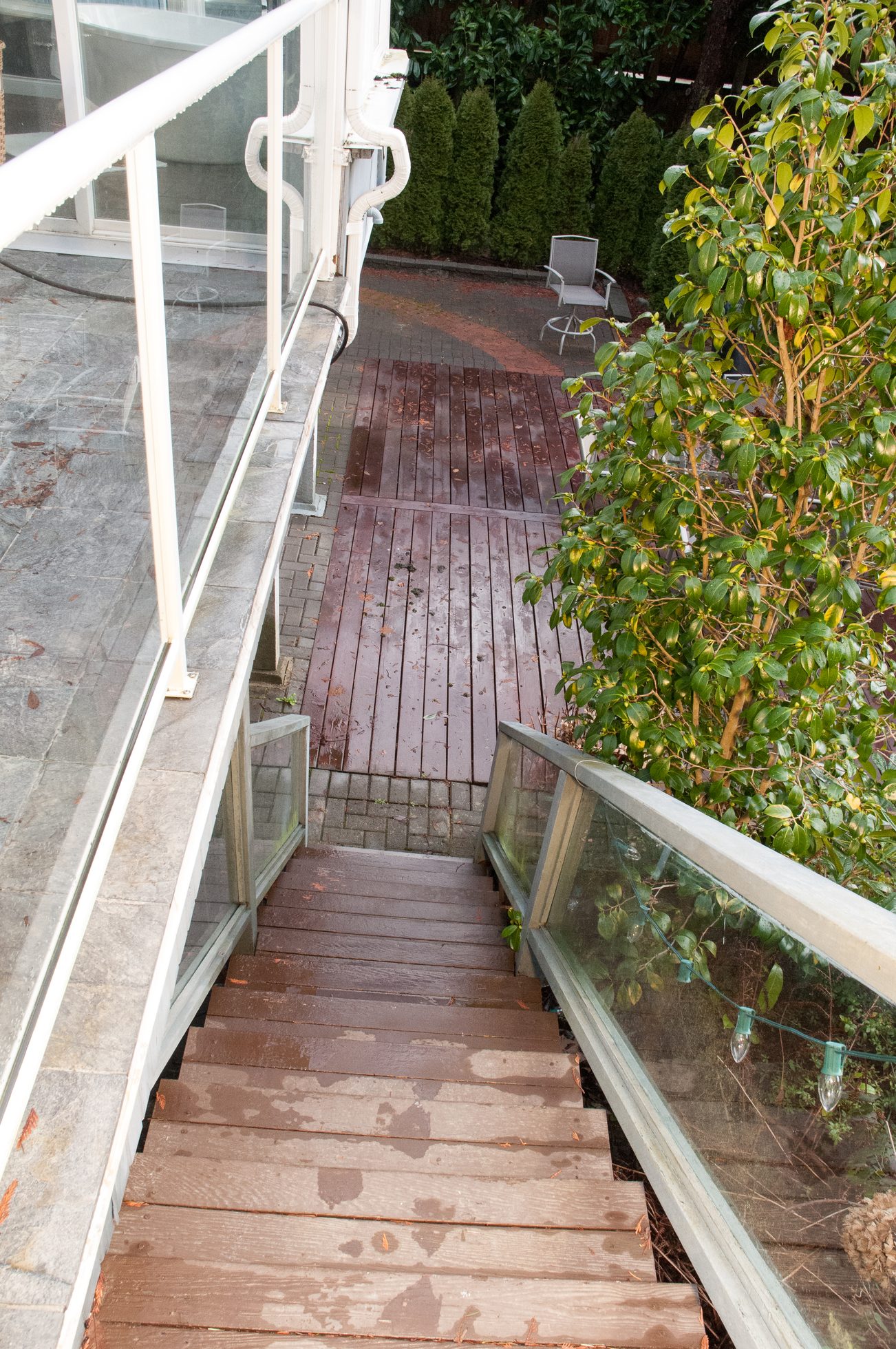 Furnished patio with wooden stairs and glass railings leading to a garden area. - 5646 Westport Rd, West Vancouver