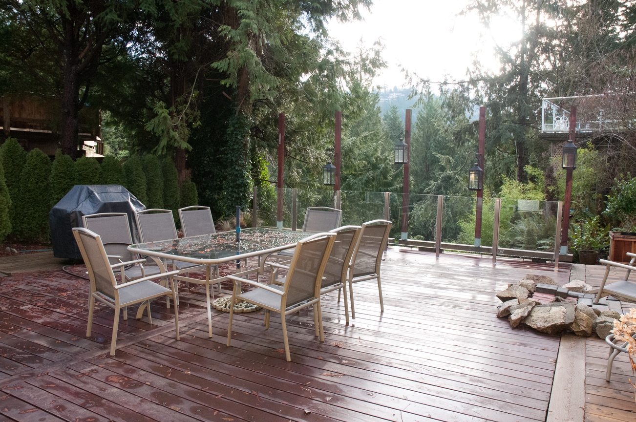 Furnished outdoor deck with glass table and chairs, surrounded by lush greenery and a view of the forest. - 5646 Westport Rd, West Vancouver