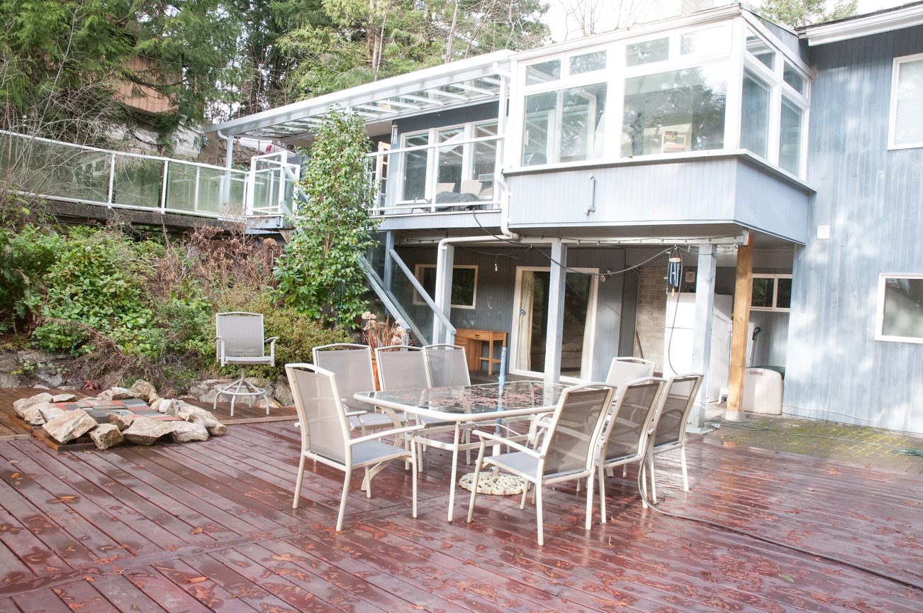 Furnished patio with glass enclosure, wooden deck, and outdoor seating. - 5646 Westport Rd, West Vancouver