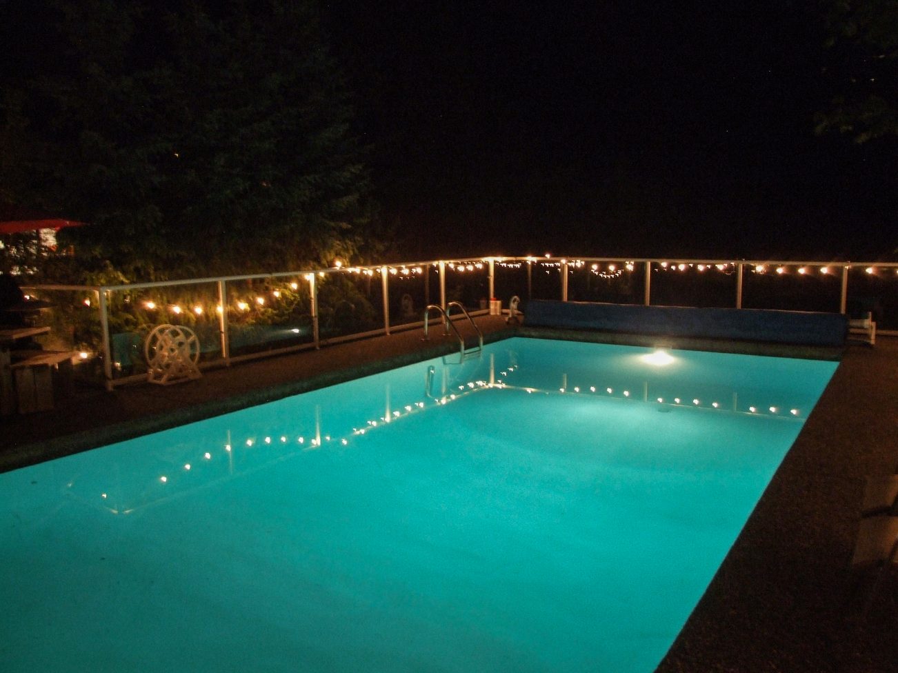 Furnished pool area with string lights and illuminated water at night. - 5646 Westport Rd, West Vancouver