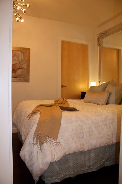 Furnished bedroom with elegant bedding and a large mirror, warm lighting, and a wooden door. - 702- 546 Beatty Street, Vancouver Downtown
