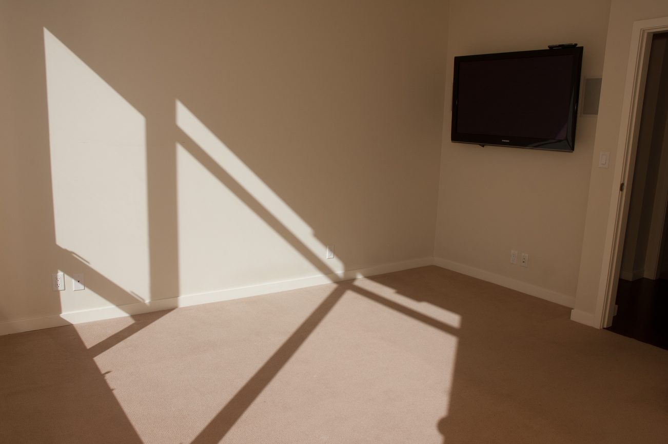 Bright living room with carpeted floor and mounted TV, shadows from window. - 100-9 Smithe Mews, Vancouver Downtown