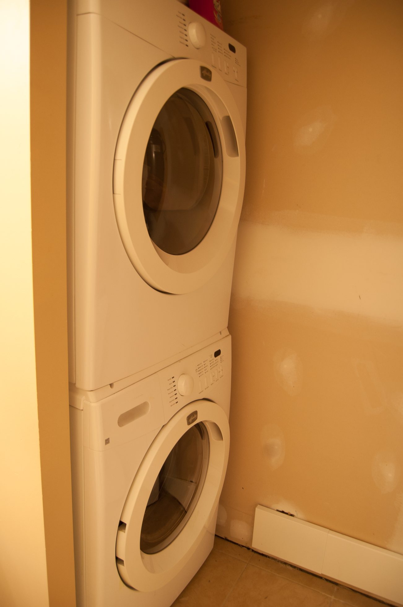 Laundry room with stacked washer and dryer, beige walls. - MAIN - 451 East Keith Road, North Vancouver