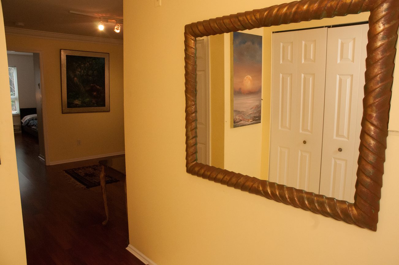 Bright living room with hardwood floors and a large mirror reflecting the room's entrance. - 204 -106 West Kings Road, North Vancouver