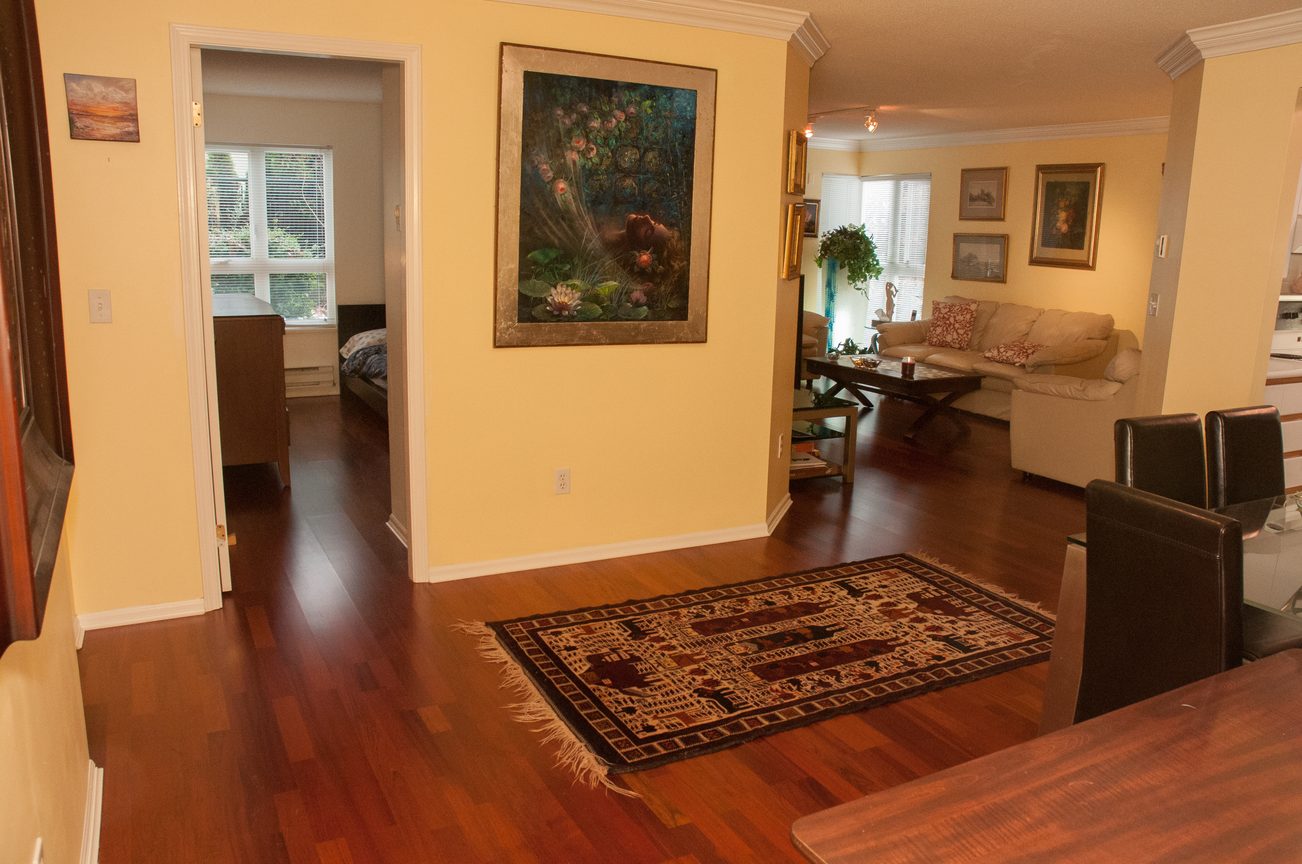 Furnished living room with hardwood floors, a large painting, and a cozy sofa. - 204 -106 West Kings Road, North Vancouver