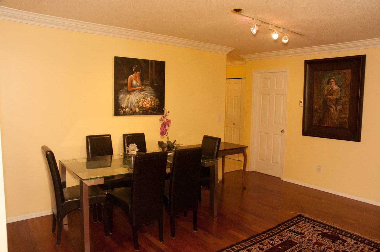 Furnished dining area with a glass table, black chairs, and wall art. - 204 -106 West Kings Road, North Vancouver