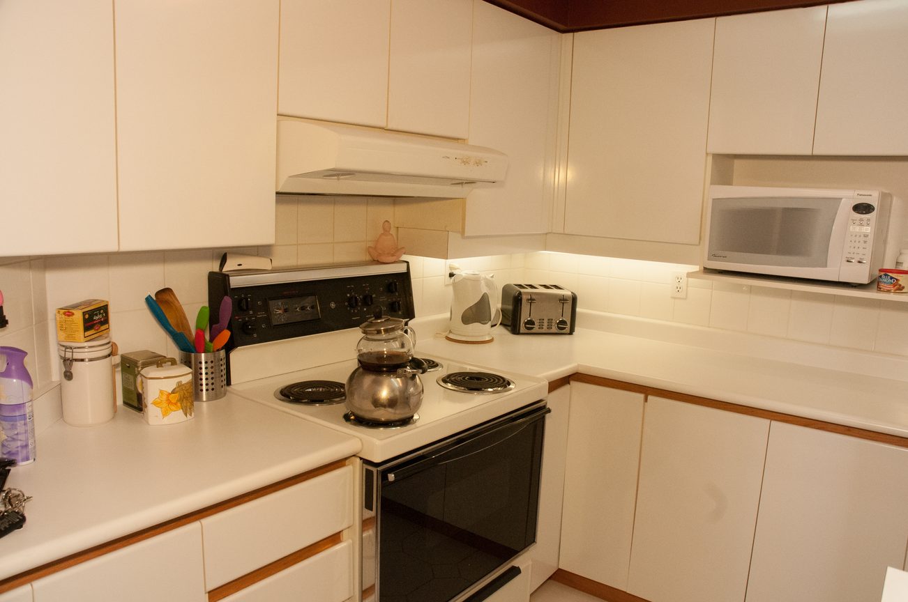 Bright kitchen with white cabinets, black appliances, and a small window. - 204 -106 West Kings Road, North Vancouver