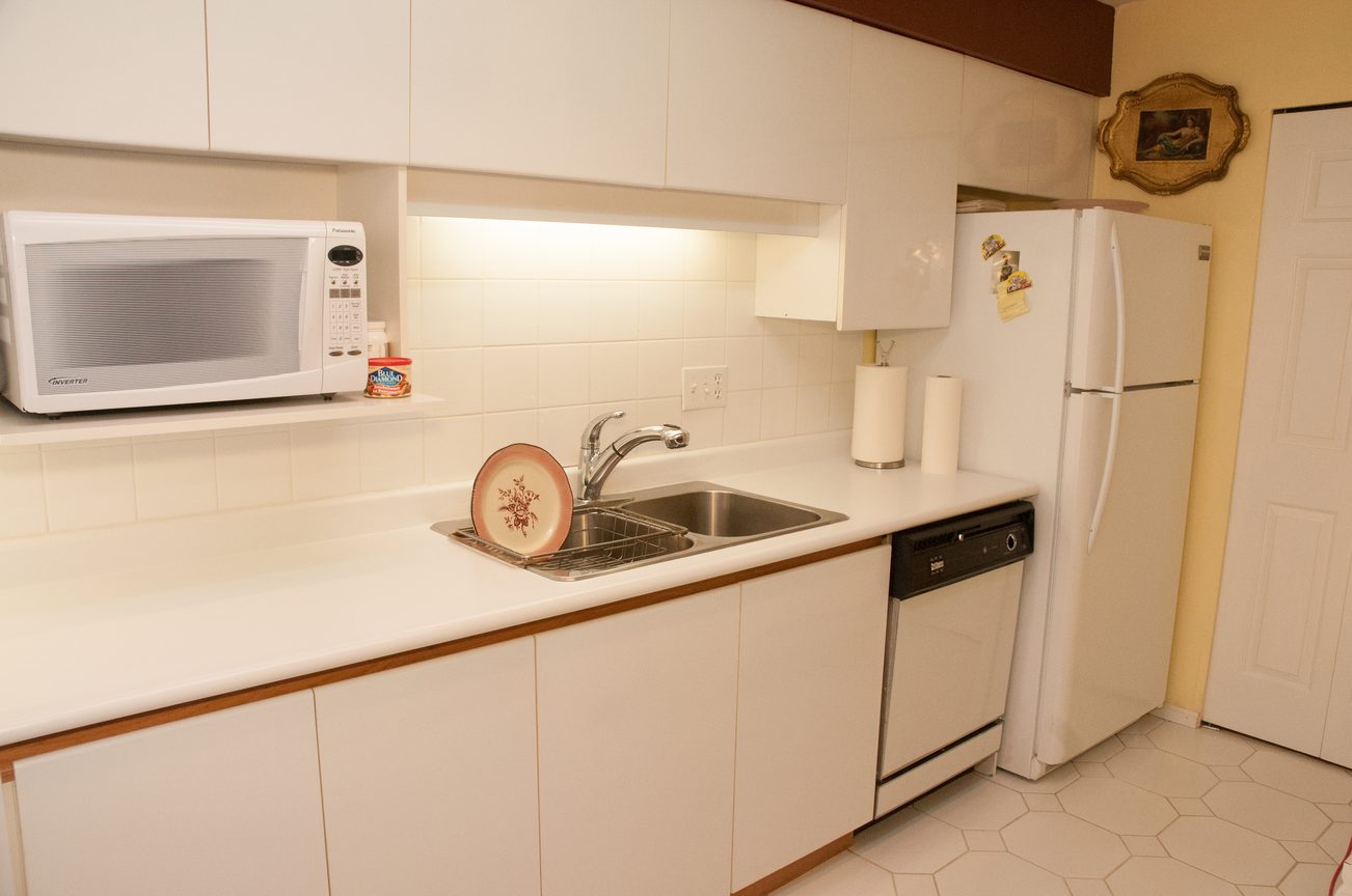 Bright kitchen with white cabinets, hexagonal tile floor, and a small microwave on the counter. - 204 -106 West Kings Road, North Vancouver