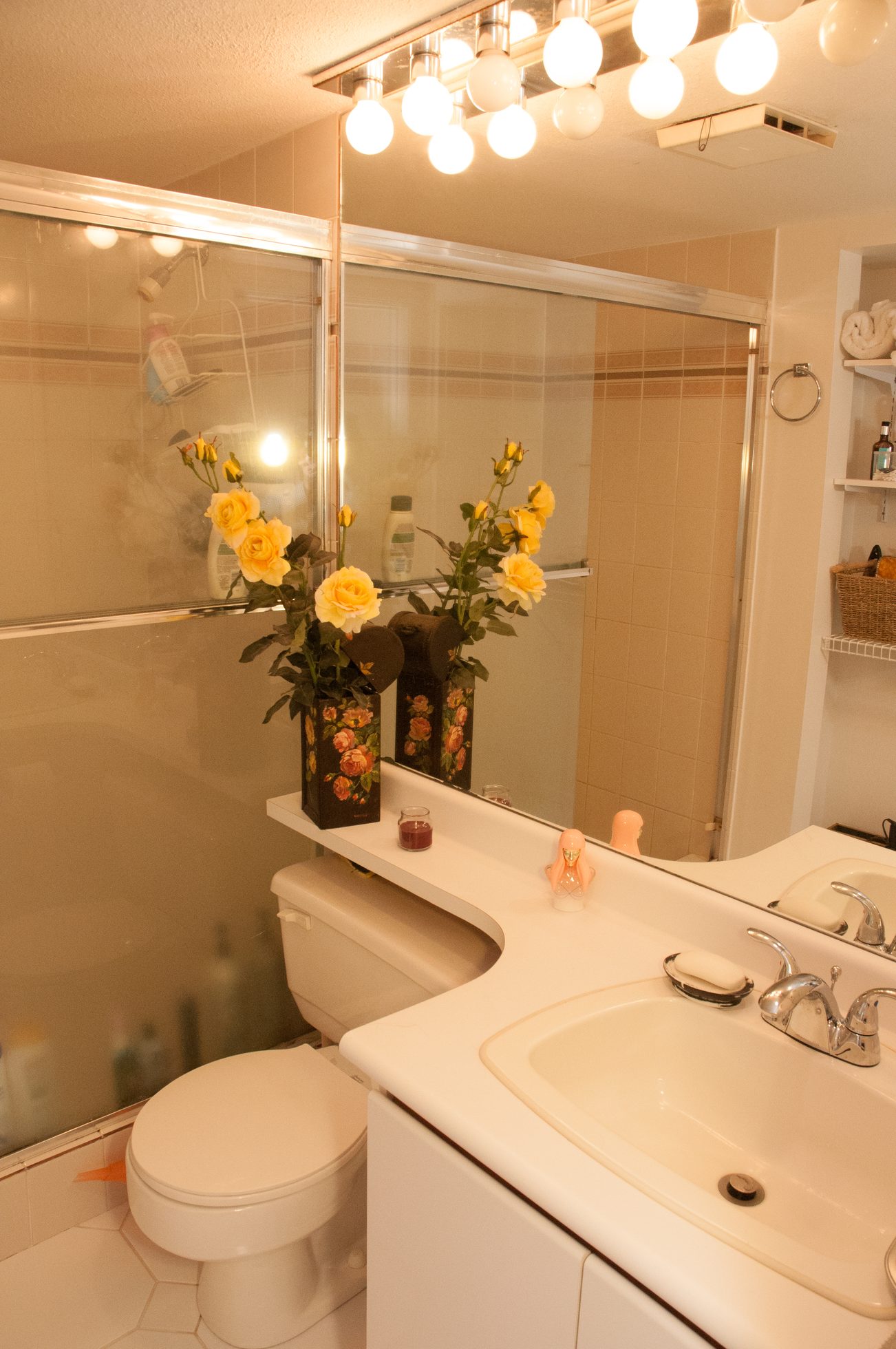 Bathroom with white countertop, yellow roses, and a sliding glass shower door. - 204 -106 West Kings Road, North Vancouver