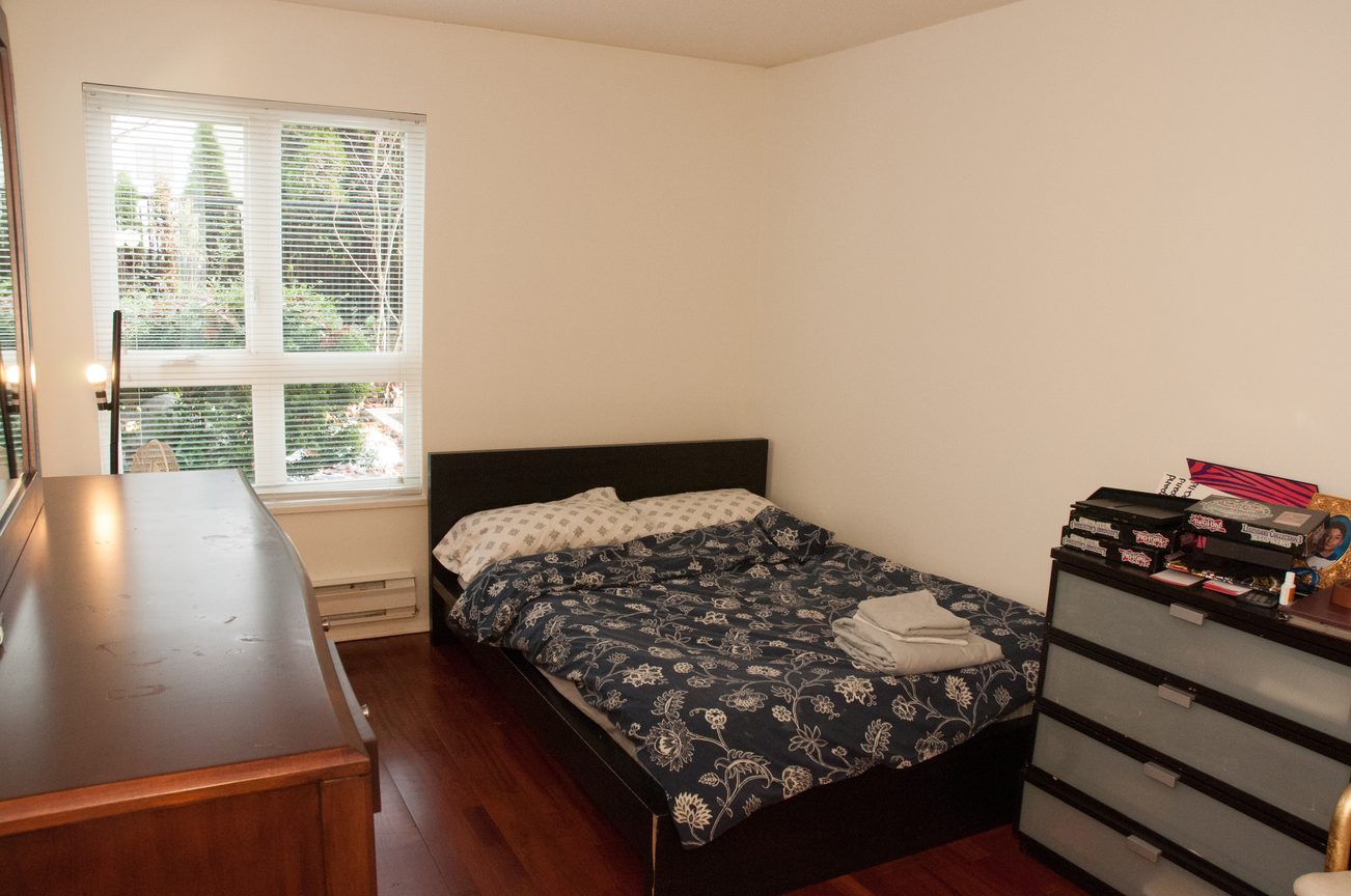 Bright bedroom with hardwood floors, dark furniture, and a window view. - 204 -106 West Kings Road, North Vancouver