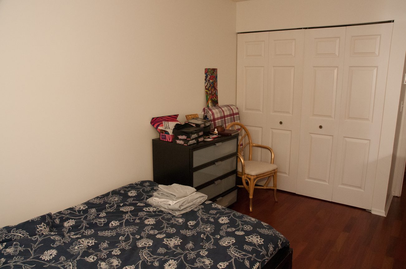 Bedroom with floral bedding, small dresser, and closet doors. - 204 -106 West Kings Road, North Vancouver