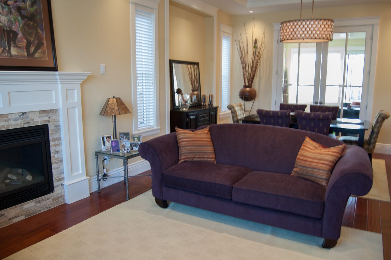 Living room with purple sectional sofa, hardwood floors, and a fireplace. - 186 West 23rd Ave, Vancouver West Side