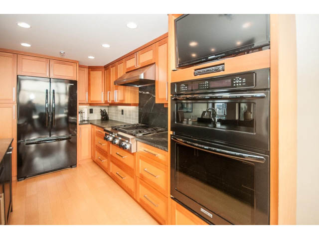Bright kitchen with black appliances, wooden cabinets, and hardwood floors. - 2901 - 1199 Marinaside, Vancouver Downtown