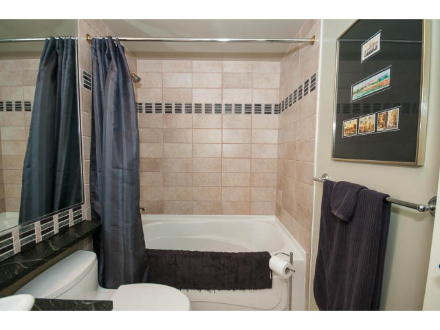 Furnished bathroom with black shower curtain, beige tiles, and dark countertop. - 2901 - 1199 Marinaside, Vancouver Downtown