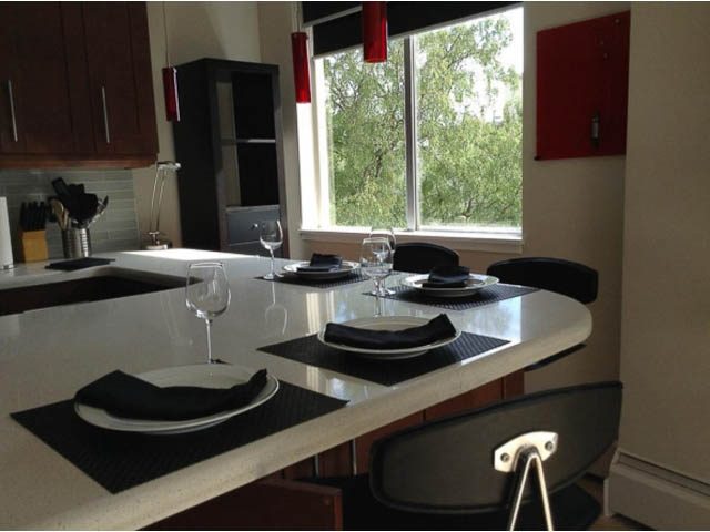 Bright kitchen with white countertops, black bar stools, and a city view through the window. - 501 - 1251 Cardero Street, Vancouver Downtown
