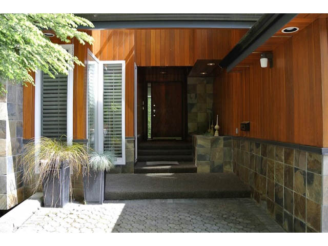 Foyer with wooden paneling and stone accents, leading to a dark entrance door. - 2450 Riverside Drive, North Vancouver