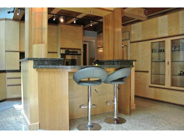 Bright kitchen with wooden cabinets, granite countertops, and modern bar stools. - 2450 Riverside Drive, North Vancouver