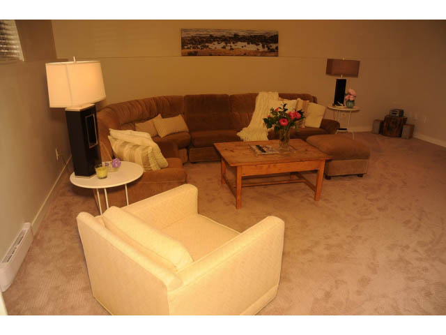 Furnished living room with beige carpet, sectional sofa, coffee table, and lamp. - Suite-942 Belvedere Drive, North Vancouver