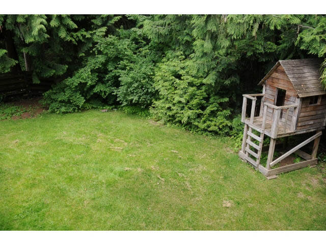Fenced backyard with wooden playhouse and lush greenery. - Suite-942 Belvedere Drive, North Vancouver